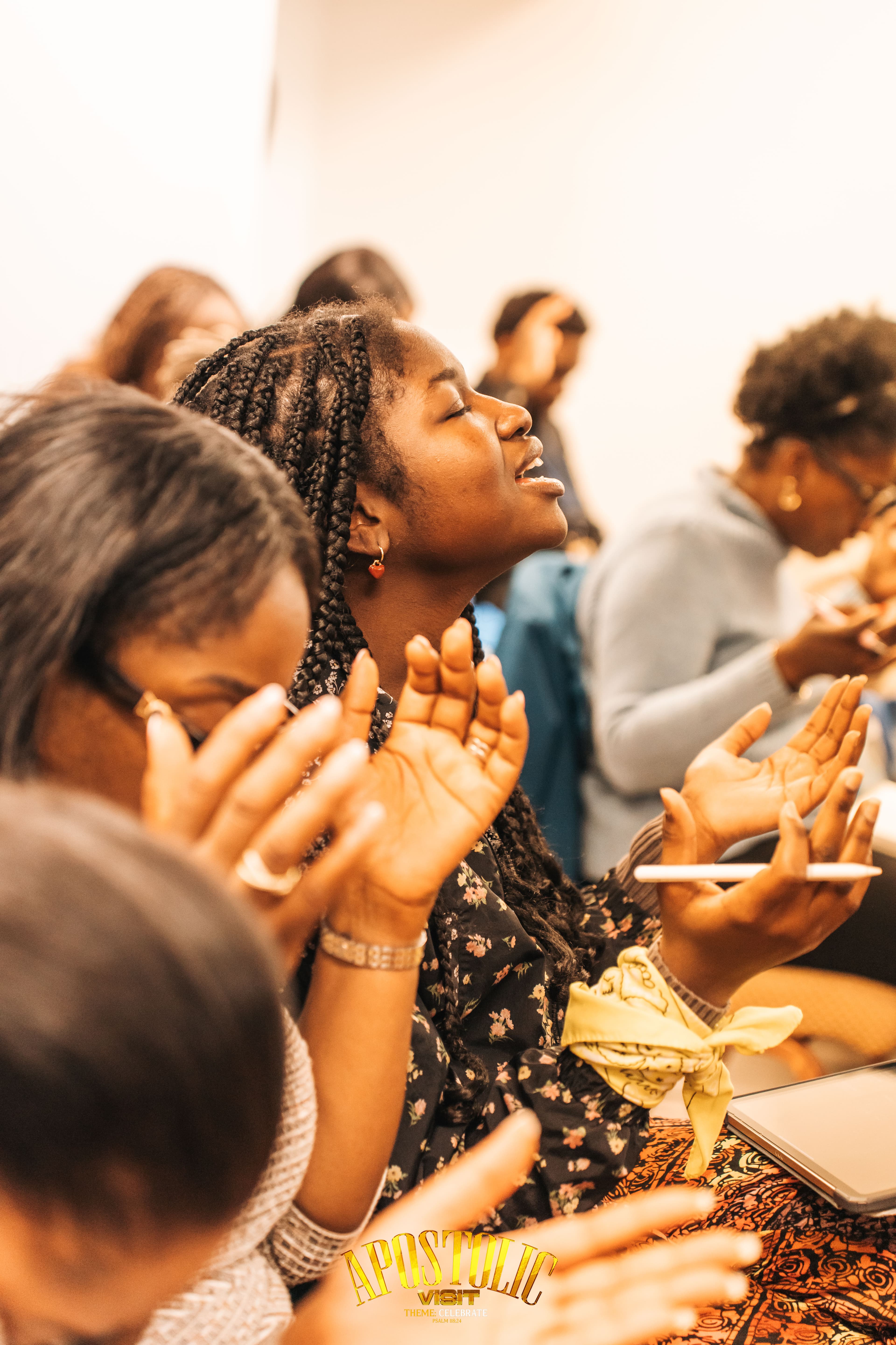Young Black woman with braids raises her hands in worship with eyes closed during service.