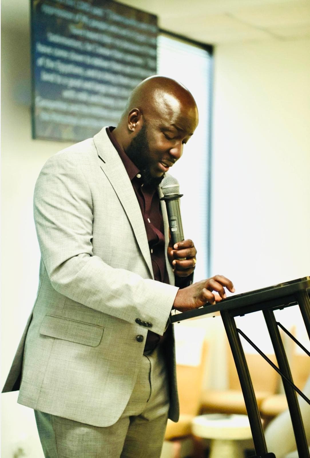 Black man in a grey suit speaking into a microphone at a black podium.